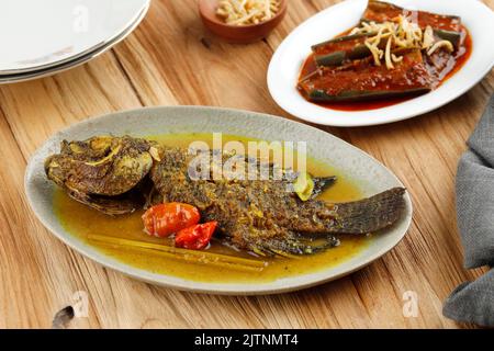 Ragoût de poisson Gourami épicé aux épices de curry jaune. Cuisine thaïlandaise et indonésienne. Sur une table en bois Banque D'Images