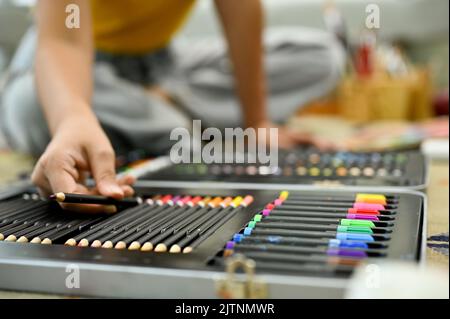 Une étudiante qui choisit une couleur de crayon pour son œuvre d'art à partir d'un ensemble de coloriage, fait ses devoirs d'art à la maison. Image rognée Banque D'Images