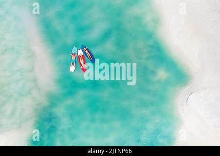 La famille se repose sur des planches Sup dans la mer turquoise. Trois personnes se trouvent dans l'océan, près de la plage. Banque D'Images