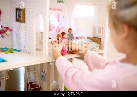 Un autre jour dans la vie des poupées. Une petite fille jouant avec sa maison de poupées à la maison. Banque D'Images