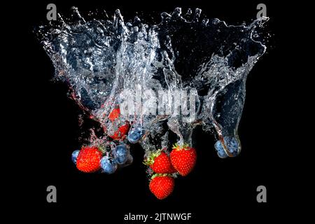 Fraises fraîches et bleuets éclaboussant sous l'eau sur le noir Banque D'Images
