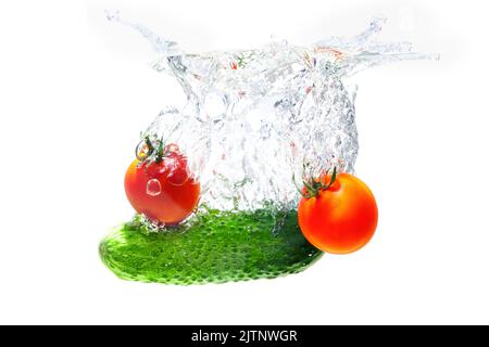 Le concombre frais et les tomates cerises tombèrent dans l'eau avec des éclaboussures isolées sur fond blanc. Banque D'Images