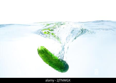 Le concombre frais est tombé dans l'eau bleue avec des éclaboussures isolées sur fond blanc. Banque D'Images