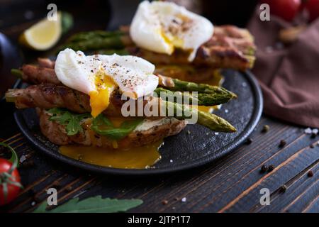 Délicieux petit déjeuner - toasts au fromage à la crème, œufs pochés et asperges enveloppés de bacon et d'épices sur une assiette Banque D'Images