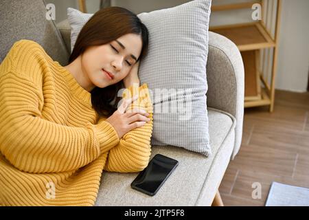 Belle palourdes jeune asiatique se détend dormant ou prenant la sieste sur son canapé confortable dans le salon minimal. Concept de repos, de sieste d'après-midi Banque D'Images