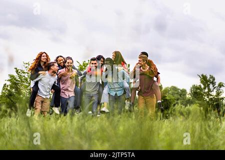 Groupe de jeunes gens joyeux et multiethniques marchant ensemble et jouant à la pigeyback dans la campagne - heureux amis ayant le plaisir de se réunir dans le weeke Banque D'Images