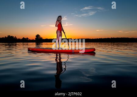 Sauvetage d'eau sur une planche à paddle debout devant le soleil couchant. Banque D'Images