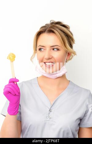 Le maître de l'enlèvement de cheveux de sucre contient de la pâte de sucre jaune liquide, de la cire pour l'épilation sur un bâton de bois sur un fond blanc Banque D'Images