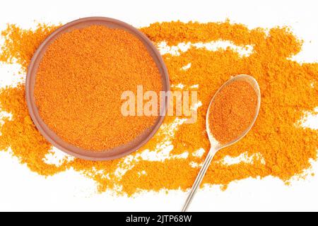 Épice au piment rouge dans une cuillère en métal et assiette en argile sur fond de piment rouge dispersé. Macro. Pose à plat. Concept de cuisine végétarienne Banque D'Images