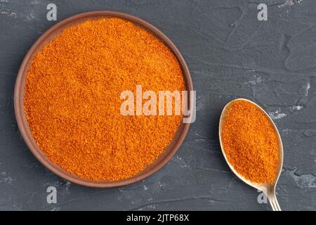 Épice au piment rouge dans une assiette en argile et cuillère en métal sur fond de béton noir. Macro. Vue de dessus. Concept de cuisine végétarienne Banque D'Images