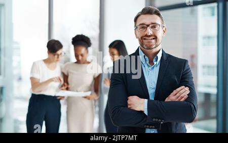 Chaque dirigeant fort a besoin de courage, de passion et d'ambition. Portrait d'un homme d'affaires mature debout dans un bureau avec ses collègues dans le Banque D'Images