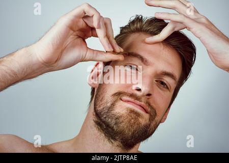 Soyez le patron de vos sourcils. Studio photo d'un beau jeune homme qui pette ses sourcils sur un fond gris. Banque D'Images