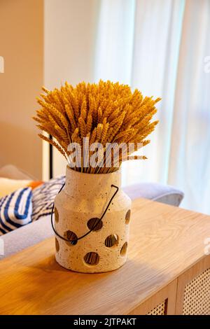 Une feuille ou un bouquet de tiges de blé séchées se tient dans un vase sur une table en bois, sur fond de rideau léger. Décoration intérieure moderne à motif ressort. flo sec Banque D'Images