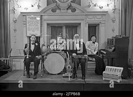 Un groupe de danse britannique de quatre pièces, avec des membres du de Berrys Trio, en scène à une œuvre caritative Benefit Dance dans le cadre de la NSPCC (la National Society for the Prevention of cruelle to Children) dans un hôtel de Londres, en Angleterre, au Royaume-Uni, en 1939. Le signe derrière le groupe demande aux danseurs de s'abstenir de «tamper et sauter». Les premiers groupes de danse et de swing ont eu leur âge d'or au Royaume-Uni durant la période 1920s-30s. Groupes joués dans les salles de danse et les salles de bal de l'hôtel. Ils jouaient de la musique mélodique et de bon temps et des joueurs individuels joueraient dans plusieurs groupes. Cette image provient d'un vieux négatif en verre – une photographie vintage de 1930s. Banque D'Images