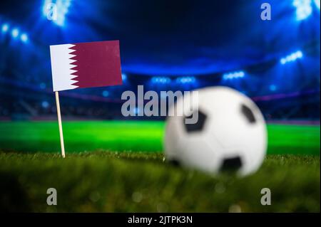 Drapeau du Qatar sur l'herbe verte du stade de football moderne la nuit. Photo de sport, espace de montage sombre Banque D'Images