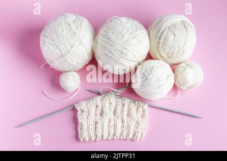 Boules blanches de fil avec aiguilles de tricotage sur un fond rose pour tricotage de vêtements chauds, passe-temps Banque D'Images