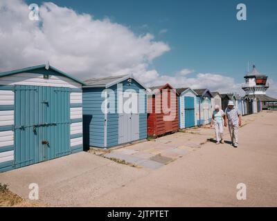 Un couple de personnes âgées qui se promeussent devant des cabanes de plage peintes sur le front de mer de Harwich, sur la côte d'Essex, en été, en Angleterre, au Royaume-Uni Banque D'Images