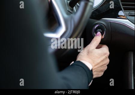 La femme démarre le moteur de la voiture avec le bouton START-STOP. Intérieur de voiture moderne, gros plan Banque D'Images