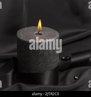 Une bougie noire qui brûle sur un fond noir Banque D'Images