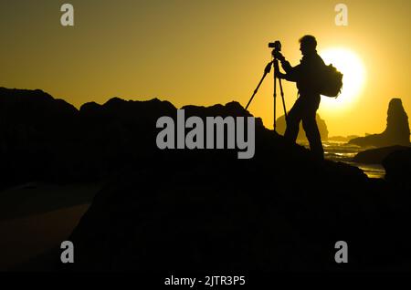 Une silhouette de photographe est entourée contre le soleil couchant à Bandon, Oregon Banque D'Images