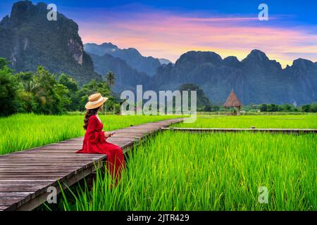 Young woman sitting on wooden path avec champ de riz vert à Vang Vieng, Laos. Banque D'Images