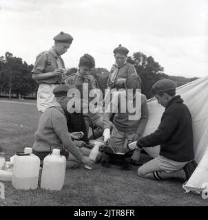 1965, historique, scouting dans le Glen, scouts de cub en uniforme et bérets, cuisine de nourriture en plein air sur l'herbe à l'extérieur d'une tente, Écosse, Royaume-Uni, semble être des omelettes... Banque D'Images