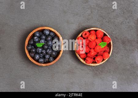 Vue de dessus bleuets et framboises frais dans des bols en bois sur fond noir. Alimentation saine, plat de nourriture végétalienne. Banque D'Images