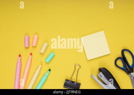 Crayons de couleur, pinces et papier à notes, ciseaux, agrafes. Retour à l'école. Arrière-plan jaune isolé Banque D'Images