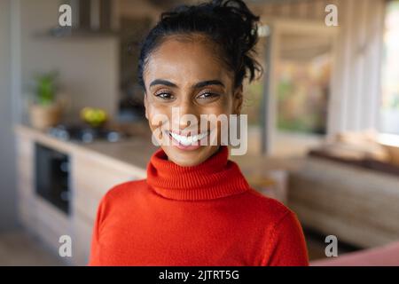 Portrait en gros plan d'une belle femme biraciale souriante de taille moyenne adulte portant un t-shirt à col roulé à la maison Banque D'Images