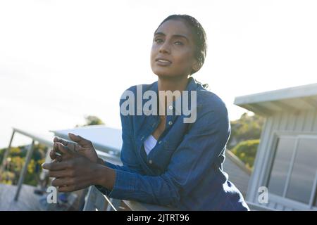 Femme biraciale moyenne adulte attenuée regardant loin tout en se penchant sur les balustrades dans le balcon, espace de copie Banque D'Images