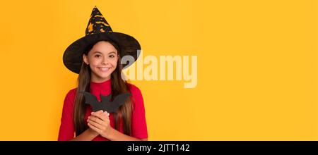 joyeux enfant avec une chauve-souris portant un chapeau de sorcière sur fond jaune, witchery. Portrait de fille d'Halloween, affiche horizontale. En-tête de bannière avec espace de copie. Banque D'Images