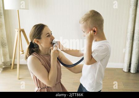 Le garçon écoute par un stéthoscope ce que sa mère lui dit. Jeux pour enfants Banque D'Images