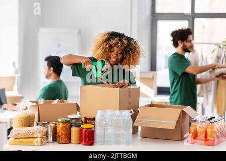 des bénévoles heureux emballant des aliments dans des boîtes de dons Banque D'Images