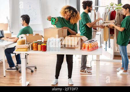 des bénévoles heureux emballant des aliments dans des boîtes de dons Banque D'Images