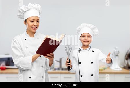 chef féminin avec livre de cuisine et fille dans la cuisine Banque D'Images