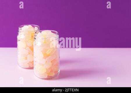 Gros plan de deux bocaux en verre remplis de bonbons gélifiants aux agrumes sur fond violet. Prise de vue en studio, mise au point sélective, espace pour le texte. Banque D'Images