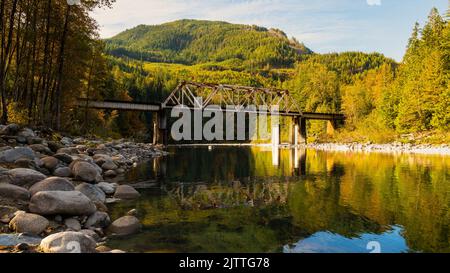 La rivière Skykomish reflète le pont ferroviaire lorsque les arbres commencent à se transformer en couleurs d'automne dans l'ouest de l'État de Washington Banque D'Images