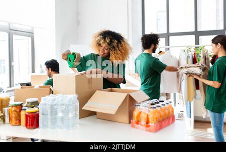 des bénévoles heureux emballant des aliments dans des boîtes de dons Banque D'Images