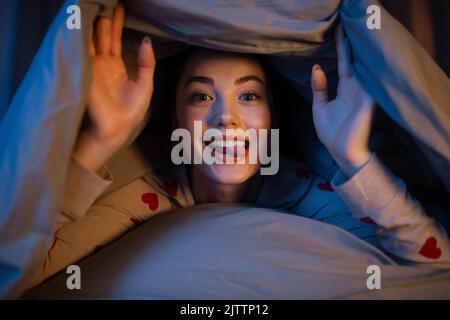 bonne adolescente couchée sous une couverture dans le lit Banque D'Images