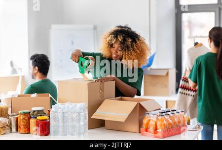 des bénévoles heureux emballant des aliments dans des boîtes de dons Banque D'Images