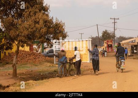 Un cycliste regarde comme trois personnes déchargent un lit d'un vélo. La bicyclette est le moyen de transport le plus courant, car elle est considérée comme moins chère que les autres modes de transport. Lilongwe, Malawi. Banque D'Images