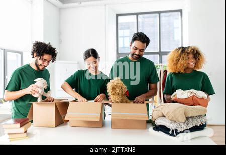 des bénévoles heureux emballant des choses dans des boîtes de dons Banque D'Images