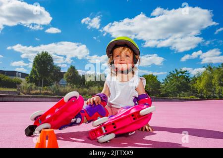 Les filles apprennent les rouleaux, s'assoient en protection sur le sol coloré du parc Banque D'Images