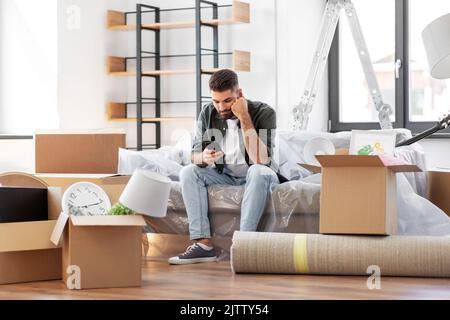 triste homme avec un smartphone et des boîtes de déménagement à la maison Banque D'Images