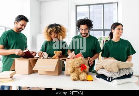 des bénévoles heureux emballant des choses dans des boîtes de dons Banque D'Images