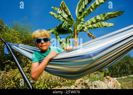 Le garçon repose dans un hamac dans le jardin au-dessus du palmier Banque D'Images