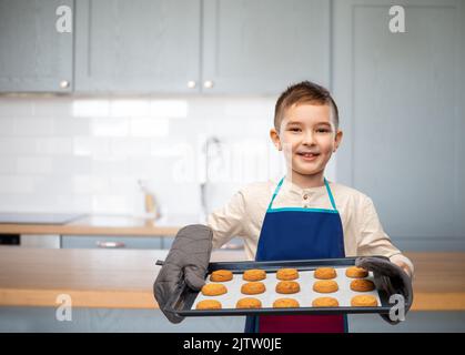 garçon dans un tablier tenant une plaque de cuisson avec des biscuits Banque D'Images