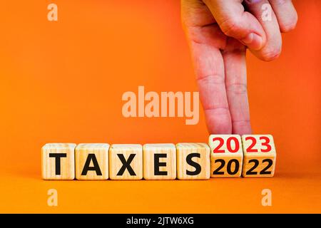 symbole 2023 taxes nouvel an. Homme d'affaires transforme un cube en bois et change les mots impôts 2022 en impôts 2023. Magnifique table orange fond orange, copie Banque D'Images