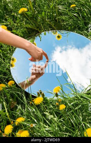 main touchant le reflet du ciel dans le miroir sur le terrain Banque D'Images