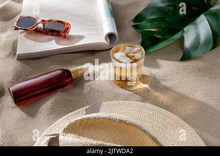 magazine, lunettes de soleil et écran solaire sur le sable de plage Banque D'Images